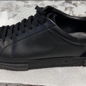 Arigato skor - Unika Axel Arigato-sneakers i svart – stilrena och exklusiva. Använt ett fåtal gånger. Levereras i originalförpackning med dust bag och allt tillbehör. Perfekt både till vardags och fest. Ta chansen att äga ett par premiumskor som sticker ut och levererar både komfort och design!