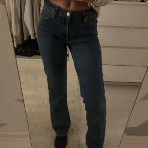 Lee blå jeans W26 L31 - Snygga blå jeans från LEE i modellen Straight med klassisk femficksdesign och låg midja. Jeansen har ett rakt ben och en liten slitning vid knät för en cool touch. Tillverkade i jeansmaterial  och knappstängning framtill. Super fina och använda fåtal gånger. Storlek W26 L31. Pris:220