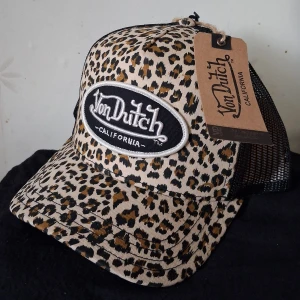 Leopardmönstrad keps från Von Dutch - Snygg keps från Von Dutch med leopardmönster i beige, svart och brunt. Framsidan har en stor broderad logga i svart och vitt, och baksidan är i svart mesh för extra ventilation. Ny, oanvänd.