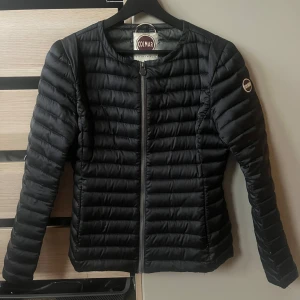 Svart dunjacka från Colmar - Snygg svart dunjacka från Colmar med quiltad design och rund hals. Jackan har en smal passform, dragkedja framtill och Colmar-logga på ärmen. Perfekt för kyliga dagar och enkel att matcha med olika outfits. Jag har bara använt den ett fåtal gånger men är som gott som ny. Kan även diskutera priset. 