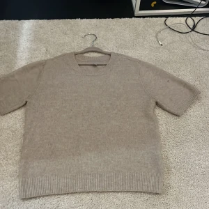 Beige stickad tröja från H&M XS - Säljer en beige stickad tröja från H&M i storlek XS. Tröjan har korta ärmar, rund hals och ribbade muddar vid ärmslut och nederkant. Perfekt för dig som gillar en enkel och chill stil med mjukt material.