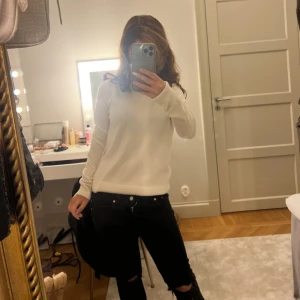 Svarta jeans med slitningar - Säljer ett par svarta jeans med snygga slitningar vid knäna. Jeansen har låg midja och klassisk femficksdesign med metallknappar och nitar. Passformen är slim och de är perfekta för en cool och avslappnad stil. Säljer då de blivit för små och de är köpta innan sommaren.