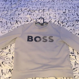 Ljusgrå sweatshirt från BOSS - Köpt för 1200, använd max 10 gånger.Snygg ljusgrå sweatshirt från BOSS med stort svart och grått logotryck på bröstet. Tröjan har rund hals, långa ärmar och mjukt material som känns skönt mot huden. Perfekt för dig som gillar stilrena och moderna plagg med tydlig branding.