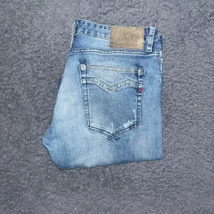 Replay jeans - Snygga Replay Newbill jeans i klassisk blå tvätt med slitningar och raka ben. Jeansen har fem fickor, läderpatch med Replay-logga bak och tydliga kontrastsömmar. Midja 44cm, längd 108cm. JAG SKICKAR EJ FLER BILDER NÄR JAG BÄR JEANSEN! för storleksguide hänvisar jag till måtten och för bättre inblick i passformen rekommenderar jag att googla på modellnamnet. Jeansen kan vara uppsydda utan att jag noterat det så kolla måtten noggrant :) 28