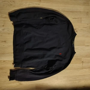 Mörkblå tröja från Polo Ralph Lauren - Mörkblå långärmad tröja från Polo Ralph Lauren med klassisk rund halsringning och röd broderad logga på bröstet. Tillverkad i mjuk bomull som är skön att ha på sig. Perfekt för en clean och stilren look. Nypris: 1250