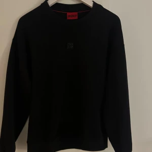 Svart sweatshirt från Hugo Boss - Köpt från farfetch Svart sweatshirt från Hugo Boss med rund halsringning och diskret logotyp på bröstet. Tröjan har en klassisk, avslappnad passform och är tillverkad i mjuk bomullsmix. Perfekt för en clean och stilren look är inte många som har just denna collection
