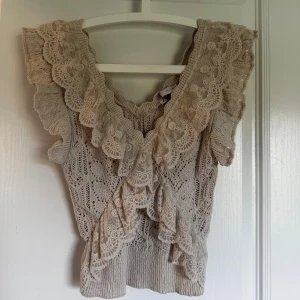 Beige spetsblus från Zara - Supersöt beige blus från Zara med breda volanger och spetsdetaljer. Blusen har v-ringad hals och är kortärmad med stickad struktur och broderade spetsmönster. Perfekt för dig som gillar romantisk och boho-inspirerad stil.
