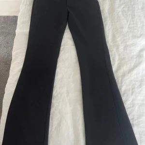 Kostymbyxor med låg midja low waist - Snygga svarta bootcut byxor med låg midja som sitter tajt över låren och har utsvängda ben. Perfekta för dig som gillar en trendig siluett och vill ha ett par stilrena byxor som funkar till många olika looks. 