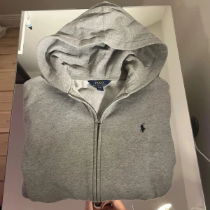 Grå hoodie med dragkedja från Polo Ralph Lauren - Säljer en klassisk grå hoodie från Polo Ralph Lauren med dragkedja och huva. Tröjan har det ikoniska broderade logotypen på bröstet och är tillverkad i mjuk bomull. Perfekt för en avslappnad stil. Storlek XL (18-20) i barnstorlek men skulle säga att den är XS-S. Jag är 171 när jag har hoodien på mig. Kom gärna med prisförslag eller frågor om det skulle vara något😀