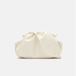 Krämvit axelväska med snörning - Snygg krämvit axelväska i mjukt skinn med cool snörningsdetalj upptill. Väskan har en rundad form och en enkel, stilren design som passar till jeans eller klänning. Perfekt storlek för mobilen och det viktigaste.