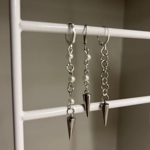 Silvriga örhängen med pärlor och spikes - Unika silvriga örhängen med kedjor, små vita pärlor och coola konformade spikes längst ner. Perfekt för dig som gillar edgy och trendiga accessoarer med en twist. Säljs som ett par. Rostfritt stål och handgjort 