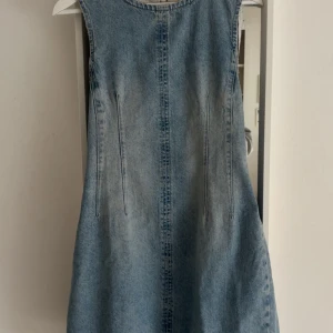 Jeansklänning från Pull&Bear i M - Säljer en ärmlös jeansklänning från Pull&Bear i storlek M. Ny med prislapp! Klänningen har en rak och enkel siluett med sömmar framtill och baktill som ger en cool vintagekänsla. Tillverkad i ljusblå denim. .