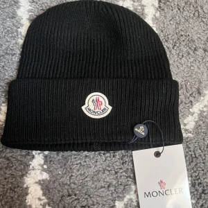 M-mössa - Säljer en svart ribbstickad mössa från M med klassisk uppvikt kant och broderad logotyp framtill. Mössan är tillverkad i mjukt ullmaterial och har en clean, stilren look som passar perfekt till kalla dagar.