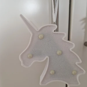 Glittrig enhörningsdekoration i vitt - Superfin enhörningsformad dekoration i vit plast med glittrig yta och pärlliknande detaljer. Perfekt att hänga upp i rummet för en magisk känsla. Drivs med batteri och har en smidig upphängningsögla.