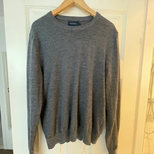 Grå merinoulltröja från Riley - Säljer en stilren grå tröja från Riley i 100% merinoull. Tröjan har rund halsringning, långa ärmar och ribbade muddar vid ärmslut och nederkant. Perfekt för lager-på-lager och passar till allt. Supermjuk och skön att bära.