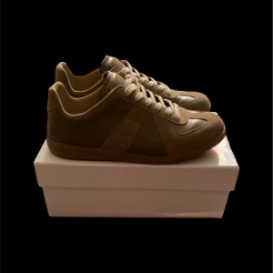 Margiela Gats  - Snygga beige sneakers med klassisk siluett och rund tå. Skorna har detaljer i mocka och skinn, samt platt sula i gummi. De har snörning framtill och neutrala färgtoner som passar till många stilar. Perfekta för dig som gillar minimalistisk design.