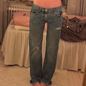 Blå ripped jeans från Gina - Säljer ett par blå jeans från Gina tricot med slitna detaljer på benen. Super snygg lite baggy/straight lågmidjad modell. Jeansen har har ett litet slit längst ner vid kanten