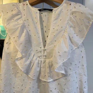 Vit blus med volang från Zara - Supersöt vit blus från Zara med broderade blommor och hålmönster. Blusen passar perfekt att klä upp eller ha till vardags! 