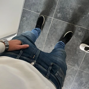 Replay Anbass  - Säljer ett par Replay Anbass jeans i slim fit, storlek 31. De är blå med snygga slitningar och klassiska fem fickor. Jeansen har låg midja och smal passform som sitter riktigt schysst. Materialet är jeans med stretch för extra komfort.