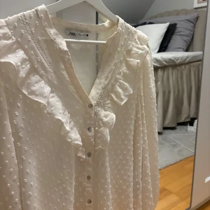 Vit blus med volanger från Zara - Supersöt vit blus från Zara med volanger längs v-ringningen och axlarna. Den här en liten defekt (se bild tre) men annars är den i fint skick! Storlek L men passar mig som vanligtvis bör S/M perfekt
