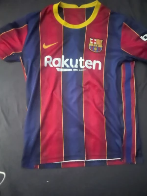 FC Barcelona - Messi- #10 Matchtröja - Passa på att köpa en av de mest eftertraktade Barcelona-tröjorna – Lionel Messi 2020/2021, hans sista säsong i klubben. En perfekt tröja för samlare, fans eller dig som vill bära en del av fotbollshistoria.  ✔ Modell: FC Barcelona Home 2020/21 ✔ Spelare: Messi #10 ✔ Storlek: (L) ✔ Skick: Godtagbart ✔ Detaljer: 	•	Det ikoniska randiga 20/21-utseendet 	•	Officiellt stilrent Messi-tryck 	•	Klara färger och bekvämt material 	•	Symbolisk säsong – Messis sista säsong i barça