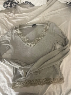 Ljusgrön spetsblus från Gina Tricot - Supersöt ljusgrön blus från Gina Tricot i storlek S. Blusen har v-ringning och är dekorerad med blommig spets vid halsringning och nederkant. Materialet är mjukt och ribbat, med långärmad passform som ger en chill vibe.