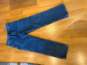 Carhartt blå jeans Single Knee Pant - Blå jeans från Carhartt, modell Single Knee Pant, med raka ben och flera praktiska fickor bak. Tillverkade i 100% ekologisk bomull, klassisk arbetsbyxstil med robust känsla. Perfekt för dig som gillar streetwear och utility-vibe. Har använts ett fåtall gånger, säljer pga. Att jag har blivit för tjock för att ha dem. Storlek 29x32