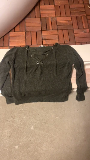 Mörkgrå stickad tröja Clockhouse M - Mysig mörkgrå stickad tröja från Clockhouse i storlek M. Tröjan har långa ärmar och snygg snörning framtill med metallöljetter. Perfekt för dig som gillar en chill och trendig look med lite extra detalj vid halsen.