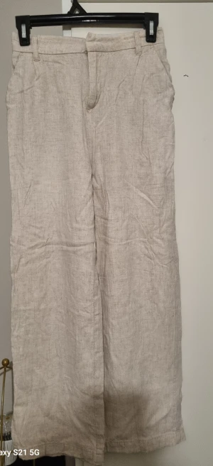 Beige linnebyxor med wide fit - Snygga beige linnebyxor med breda ben och klassisk midja. Byxorna har hällor för bälte och diskret dragkedja framtill. Perfekta för en chill och stilren look under varmare dagar.