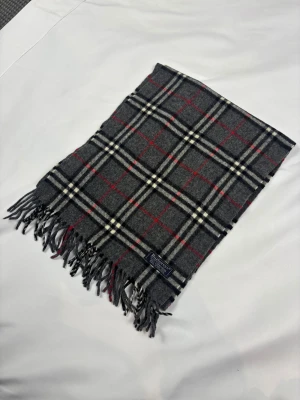 Grå Burberry halsduk - Burberry-halsduk ⭐ Superfin kvalitet, väldigt mjuk och varm – perfekt till både vardag och finare tillfällen!  ✅ I mycket gott skick ✅ Färg: Grå med klassiskt rutmönster ✅ Material: 100% Ull  Mått 📏 Längd: 150 cm Bredd: 30 cm  Hör av dig vid fler frågor! Skickas snabbt och välpackat ❤️                                                                                      N1