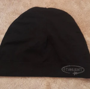 Svart mössa från Starlight - En stilren svart mössa från Starlight med diskret logga broderad i grått framtill. Enkel och klassisk design som passar perfekt när du vill hålla dig varm och samtidigt se cool ut. Mjuk och skön passform.