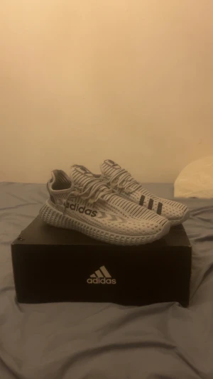 Adidas -Skor  - Produktbeskrivning – Adidas träningssko i stickad design  Upplev komfort, stil och funktion i ett med dessa moderna Adidas-skor, perfekta för både vardag och lättare träning. Skorna har en flexibel, stickad ovandel som formar sig efter foten och ger en strump-liknande passform. Det andningsbara materialet håller fötterna svala samtidigt som strukturen ger stabilitet där det behövs.  Den mönstrade yttersulan är framtagen för att ge bra grepp och dämpning vid varje steg, medan den ribbade mellansu