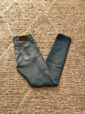 Jack&Jones jeans - Hej jag säljer ett par Jack&Jones jeans med unika slitningar i riktigt snygg ljusblå färg perfekt för dig som vill ha ett par kvalitetsjeans med grym passform, jeansen är i stretch material så otroligt bekväma. Nypris ≈ 800kr, mitt pris 299kr. Skick: 9/10 Storlek: W33L34 Midja: 40cm Lår: 23cm  Ytterlängd: 108cm Innerlängd: 85cm. Skriv gärna om du vill ha fler bilder eller har frågor!