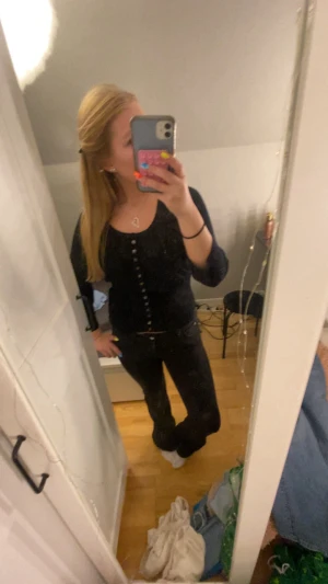 Svart kofta med knappar - Säljer en svart kofta med långa ärmar och knappar hela vägen framtill. Knapparna är blommor. Snygg och enkel modell som sitter figurnära och passar perfekt till jeans eller kjol. Koftan har en klassisk rund halsringning och är gjord i ett mjukt material.