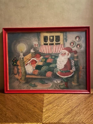 Jul tavla  - Det här är en tavla med jultema, där en tomte står bredvid en säng med två sovande barn i ett mysigt rum. Bilden har en varm och nostalgisk känsla, perfekt för att skapa julstämning. Passar dig som gillar klassiska julmotiv och vill dekorera ditt rum på ett unikt sätt. Trä ram rödmålad. 