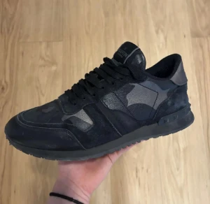 Valentino Rockrunner sneakers svart camo - Snygga Valentino Rockrunner sneakers i svart med coolt camouflagemönster. Skon har en mix av mocka och skinn, samt svarta snören och en platt sula. Perfekt för dig som vill sticka ut med en exklusiv och urban look. Skriv om ni vill ha fler bilder.