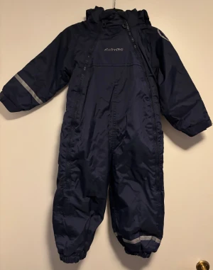 Overall strl 92 - Säljer en mörkblå overall (från Booztlet) med huva och två dragkedjor framtill. Väldigt praktisk då man kan öppna hela framsidan och lätt klä på barnet. Denna varma overall har ett mjukt fleecefoder som ger komfort under utomhuslek. Overallen har reflexdetaljer på ärmar och ben, samt elastiska muddar vid handleder och anklar. Vattentät med 10 000 mm vattenpelartryck. 
