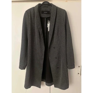 Glittrig kavaj från Vero Moda - Snygg kavaj från Vero Moda i svart och silver med glittrig finish. Kavajen har lång ärm och en rak, stilren siluett med knappar framtill. Perfekt för dig som vill sticka ut med en elegant look och glittra lite extra. 