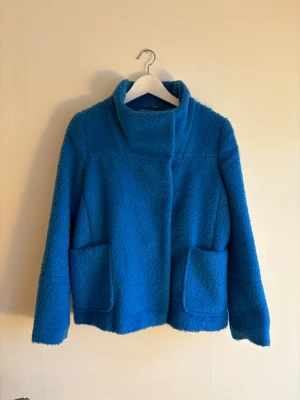 Blå teddyjacka från Atmosphere - Säljer en blå teddyjacka från Atmosphere i storlek 34. Jackan har en hög krage, två stora fickor framtill och är tillverkad av en mjuk mix av polyester, viskos, akryl och ull. 