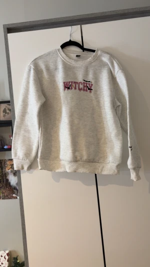 Vit sweatshirt med Witchy-tryck S - Vit sweatshirt i storlek S med trycket 'WITCHY' i rosa och svarta fladdermöss på bröstet. Mjuk bomullskänsla, rund hals och långa ärmar med broderade fladdermöss på ena ärmen. Perfekt för dig som gillar lite spooky vibes.