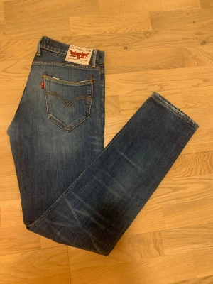 Levi's blå jeans straight fit - Snygga klassiska blå jeans från Levi's med straight fit och normal passform. Jeansen har fem fickor, gul kontrastsöm och ikonisk röd Levi's-tab på bakfickan. Tillverkade i slitstarkt denim med coola slitningar och detaljer. 98% bomull,2% elastan 
