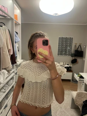 Vit stickad blus med volang från Zara🤍 - Superfin vit stickad blus från Zara med korta ärmar och bred volang över axlarna. Blusen har ett detaljerat hålmönster och ribbad halsringning. Materialet är mjukt och känns luftigt, perfekt för vår och sommar. (Andra bilden är inte min)