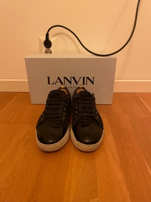 Marinblå sneakers från Lanvin - Snygga mörkblåa sneakers från Lanvin med blank tå i skinn och klassisk rund form. Skorna har mörkblåa snören, metallöglor och vit platt sula med Lanvin-logga undertill. Perfekt för dig som gillar stilrena och lyxiga sneakers med exklusiv känsla. Storlek är UK8 och EU43. Box och dustbags ingår såklart☺️