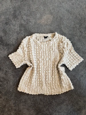 Beige ribbad topp - Säljer en beige topp från Lindex med korta ärmar och rutig textur över tröjan. Är lite mindre i storleken även fast att det är en L, skulle såga att det är mer en S. Perfekt för dig som gillar neutrala färger och vill ha något som sticker ut lite.