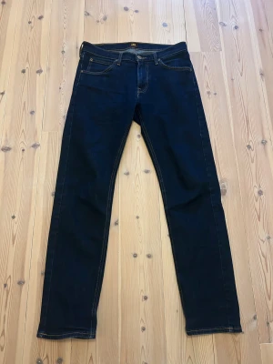 Mörkblå Lee Daren jeans W31 L32 - Säljer ett par mörkblå Lee Daren jeans med klassisk femficksmodell och gul kontrastsöm. Modellen har rak passform och dragkedjegylf. Snyggt Lee-läderpatch bak i midjan och diskret Lee-märke på bakfickan. Perfekta till en avslappnad streetstil.