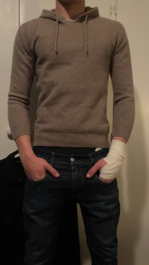 Beige hoodie i kashmir med huva - Säljer en beige hoodie i mjuk kashmir med huva och snörning. Tröjan har långärmade och ribbade muddar vid ärmslut och nederkant. Perfekt för dig som gillar chill och stilren look. Passar dig som vill ha en hoodie som är både skön och snygg.