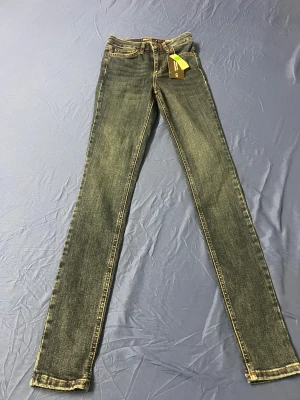 High Waist Hannah skinny jeans blå - Snygga blå jeans från Unique Denim, modell High Waist Hannah. De har hög midja, skinny fit och klassisk femficksdesign. Jeansen är tillverkade i stretchigt denim för extra komfort och har kontrastsömmar och metallknappar med logga.