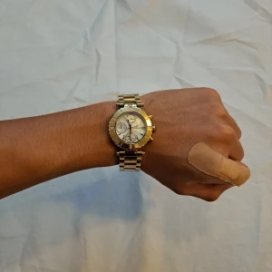 Guldfärgad klocka från Essence - Snygg guldfärgad klocka från Essence med metallarmband och rund urtavla. Urtavlan har flera små visare för dag och tid, romerska siffror och detaljer med små stenar. Perfekt accessoar för dig som gillar stilrena och lyxiga detaljer.