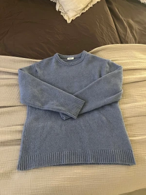 Blå stickad tröja från Kappahl - Mysig blå stickad tröja från Kappahl i storlek 146/152. Tröjan har rund hals, långa ärmar och ribbade muddar vid ärmslut och nederkant. Perfekt för kyliga dagar och enkel att matcha med jeans eller kjol.
