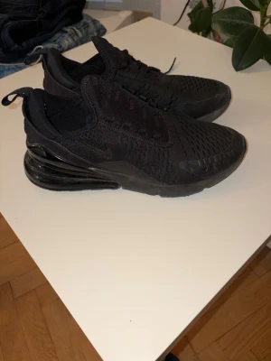 Svarta Nike Air Max 270 sneakers - Säljer ett par helsvarta Nike Air Max 270 sneakers med mesh-ovandel och stor synlig Air-enhet i hälen. Skorna har snörning, rund tå och en sportig vibe. 